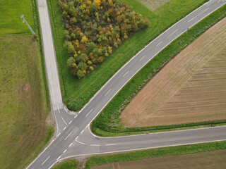 Shot from above of a road crossing between trees, grass and plowed agricultural fields in the...
