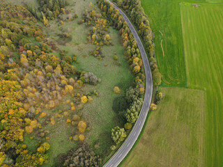 View from above of a winding road in the countryside between trees and grassland on a sunny day in autumn