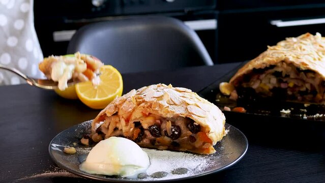 Delicious fresh strudel stuffed with apples and raisins, served with a ball of ice cream, beautiful dessert, black background