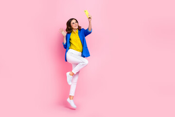 Full size photo of cheerful excited girl jumping hold telephone take selfie arm waving isolated on pink color background