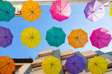Fototapeta na wymiar Multi-colored umbrellas hang on the street along the houses against the sky.