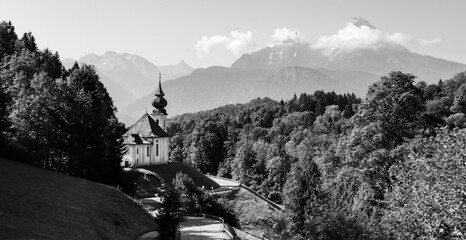 Alpine summer Panorama at “Maria Gern“ with small baroque pilgrim Chapel or church near Berchtesgaden bavaria Germany. Mountain scenery with famous Watzmann peaks in the background, black and white.