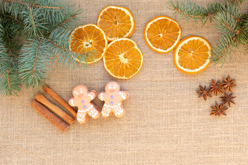 Obraz na płótnie Canvas Top view flat lay of Christmas spices for traditional beverages: cinnamon sticks, anise stars, dry orange slices as a frame for Xmas seasonal decorations on burlap fabric background with copy space