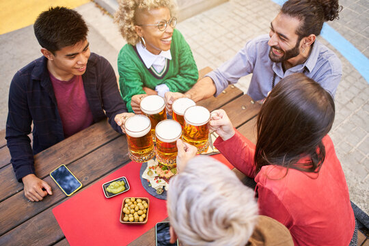Friends drinking beer at terrace outdoors on weekend. Friendship concept with young people having fun together toasting brew pint on happy hour at pub - Focus on glass. High quality photo