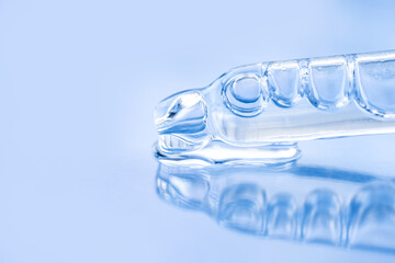 Cosmetic liquid and glass pipette close-up on a blue background. Macro photography, side view, space for text.