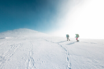 Two women on a winter hike. Girlfriends with trekking sticks go along a snow-covered mountain path....