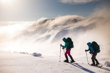 two girls with a backpack and snowshoes walk in the snow during a snow storm.
