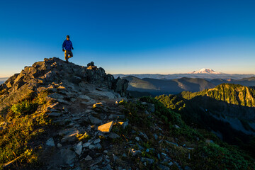 Athletic adventurous male hiker, hiking up a ridge on top of a mountain with Mount Rainier in the...