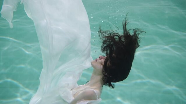 underwater shooting of a girl in a white cloth with black hair, a person slowly submerging underwater, with a caustic light effect