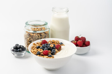 Granola with oatmeal, hazelnuts, raspberries, blueberries and yogurt in white bowl on light...