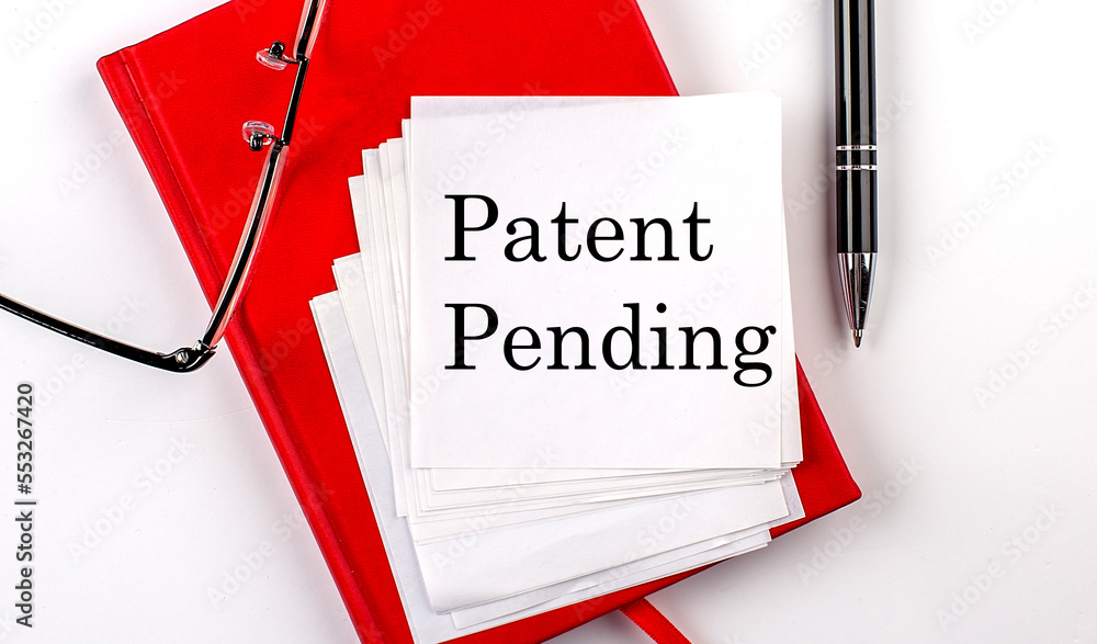 Poster patent pending text on sticker on red notebook with pen and glasses