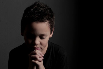 little boy praying to God with hands together with black background stock photo