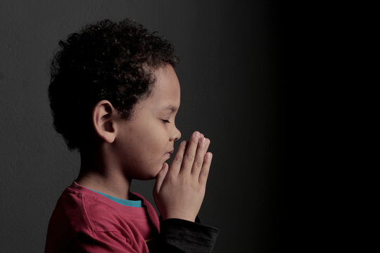 little boy praying to God with hands together with black background stock photo