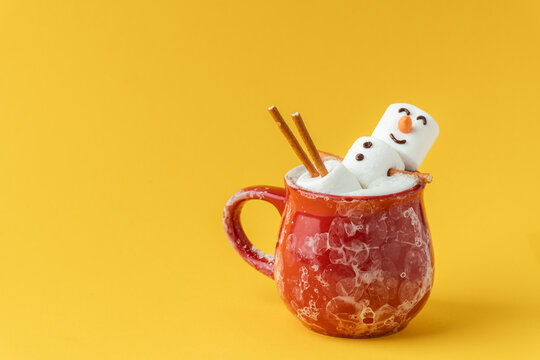 Marshmallow snowman taking hot tub in a red ceramic cup full of cocoa with milk foam. Christmas holidays yellow background. Wintertime concept. Hot chocolate with marshmallow and festive decoration.