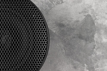 Stylish car audio acoustic round speaker with waffle grill protector cover on on gray concrete background closeup. Modern music texture