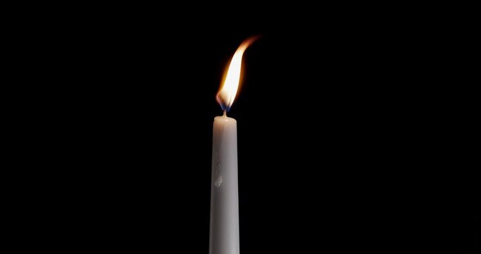 A single white candle burning. Isolated candle slow motion burning with dark background. White paraffin candle with yellow shades burns on a black background. Slow motion.
