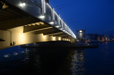 Fototapeta premium Cold dark Bosphorus sea under Galata bridge with evening city lights on a winter night. Cinematographic long exposure