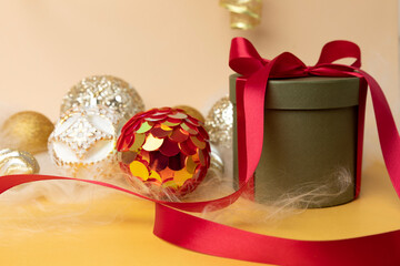 Fototapeta na wymiar New Year and Christmas background. Christmas golden balls and green round gift with red ribbon on a yellow background with angel hair. Front view