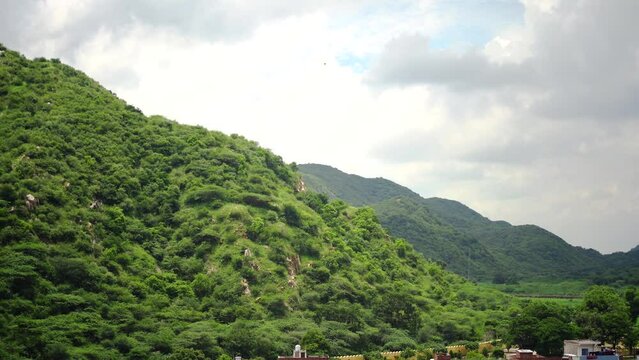 Panning shot of Aravalli range in jaipur rajasthan with small hills mountains covered in green trees under monsoon clouds