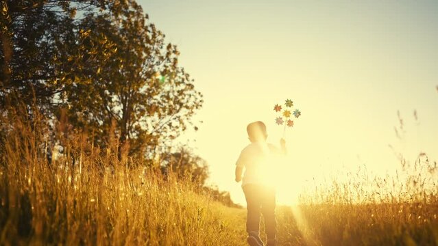 baby pinwheel. little boy silhouette plays with windmill a toy wind in the park. happy family childhood dream concept. boy play spinner toy glare of the sun at sunset fun in cheerful park