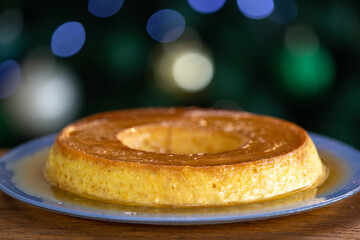 Typic caramelized condensed milk pudding with eggs, in selective focus on a blurred background of decorated Christmas tree. 