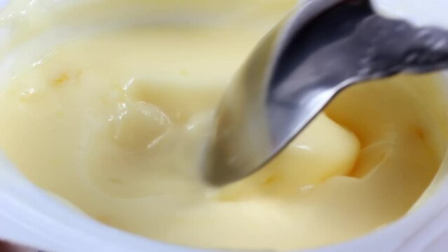 Metal spoon taking creamy yellow banana fruit yogurt close up