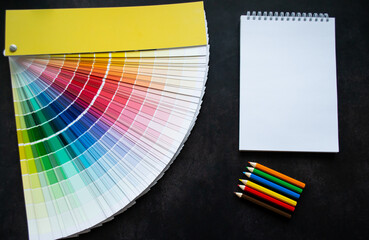 Paper fan paint swatch interior design, wall painting. Black background. White notebook, multicolored pencils, copy space