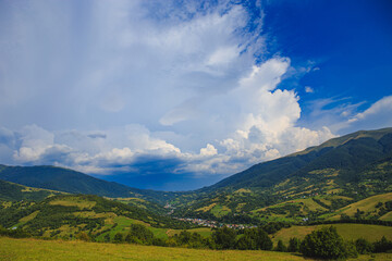 Obraz premium The mountains are covered with forests in the lowlands of the mountains village. Rural mountainous area on a sunny day with clouds.