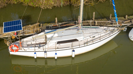 Aerial view of a white sailboat. The boat is empty and anchored at the dock. Aft mounted a solar...