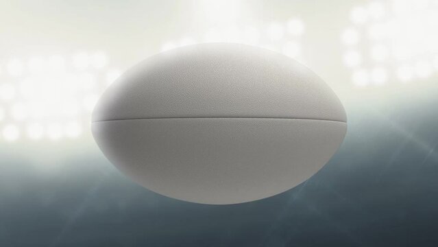 A seamlessly loop able animation of a white textured rugby ball spinning and rotating on floodlit stadium background in the night time