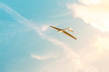 Glider flying against the blue sky with clouds and sunlight