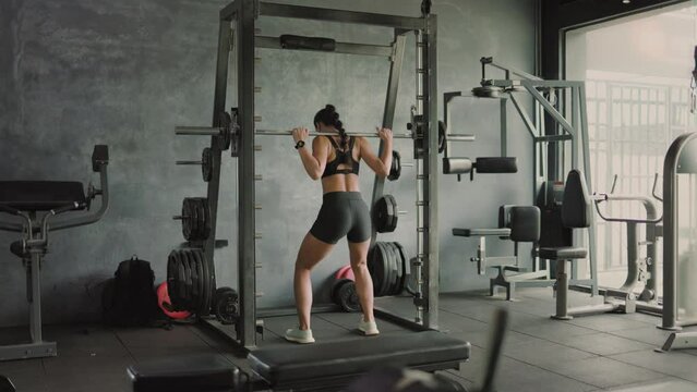 Asian female athlete doing squats in gym with barbell