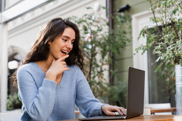 Smart girl student with laptop study english online and writting notes at linguistic school outdoor in cafe. Attractive young woman have video communication lesson with teacher.