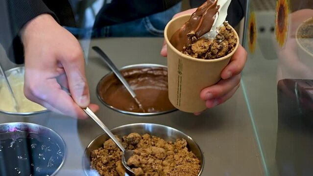 Vienna, Austria, August 2022. Slow motion footage in the Naschmarkt market. Close up shot on a frozen yogurt being garnished with different toppings by the seller.