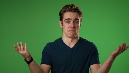 Portrait of happy young man 20s shrugging shoulders and gesturing I do not know isolated on green...