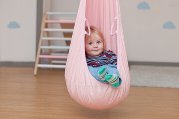 cute little boy in child cocoon hammock at home or kindergarden. toddler or kid in festive room. portrait