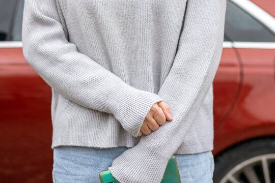 women in winter gray sweater outside in front of lateral vehicle door with collar covering nose eyes looking down.girl hand pointing something at camera,leg up holding tight hands or using smartphone