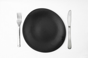 irregular round black plate with silver fork and knife on white