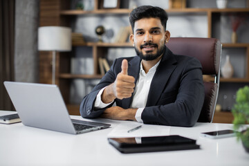 Confident young middle eastern businessman sitting at work table at modern office, typing on...