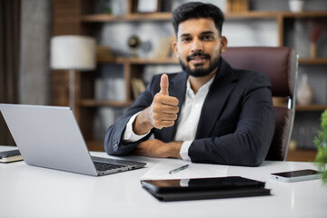 Confident young middle eastern businessman sitting at work table at modern office, typing on...