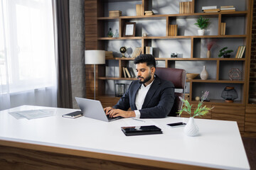 Successful bearded businessman in stylish uit working on laptop computer on modern office....