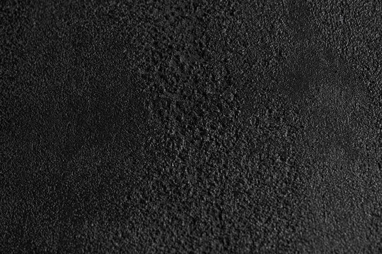 Close up of dark grey, grainy surface for modern, unusual background design. Rough texture of black covering backdrop. Concept of textures and background.