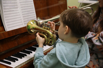 A child playing the trumpet with a teacher studying in class while standing at the piano