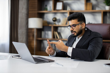 Fototapeta na wymiar Young bearded businessman using laptop computer during video call working in office. Concentrated adult successful man wearing official suit sitting at wooden desk indoor.