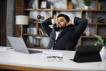 Confident man in glasses sitting relax at home office workplace take nap or daydream. Happy relaxed Caucasian young male rest in chair distracted from computer work, relieve negative emotions.