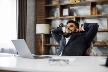 Obraz premium Confident man in glasses sitting relax at home office workplace take nap or daydream. Happy relaxed Caucasian young male rest in chair distracted from computer work, relieve negative emotions.
