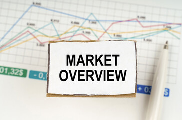 Against the background of business graphics and pens, a sign with the inscription - MARKET OVERVIEW