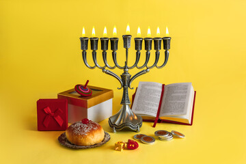 Image of Jewish holiday Hanukkah with menorah (traditional Candelabra), donuts and wooden dreidels (spinning top), doughnut, chocolate coins on a yellow background.