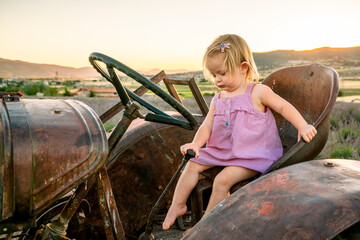 A small child farmer operates agricultural machinery. Cute girl on an old tractor