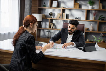 Back view of two business people, man and woman, representing sides of contract, sitting opposite each other at table discussing deal during meeting in office.
